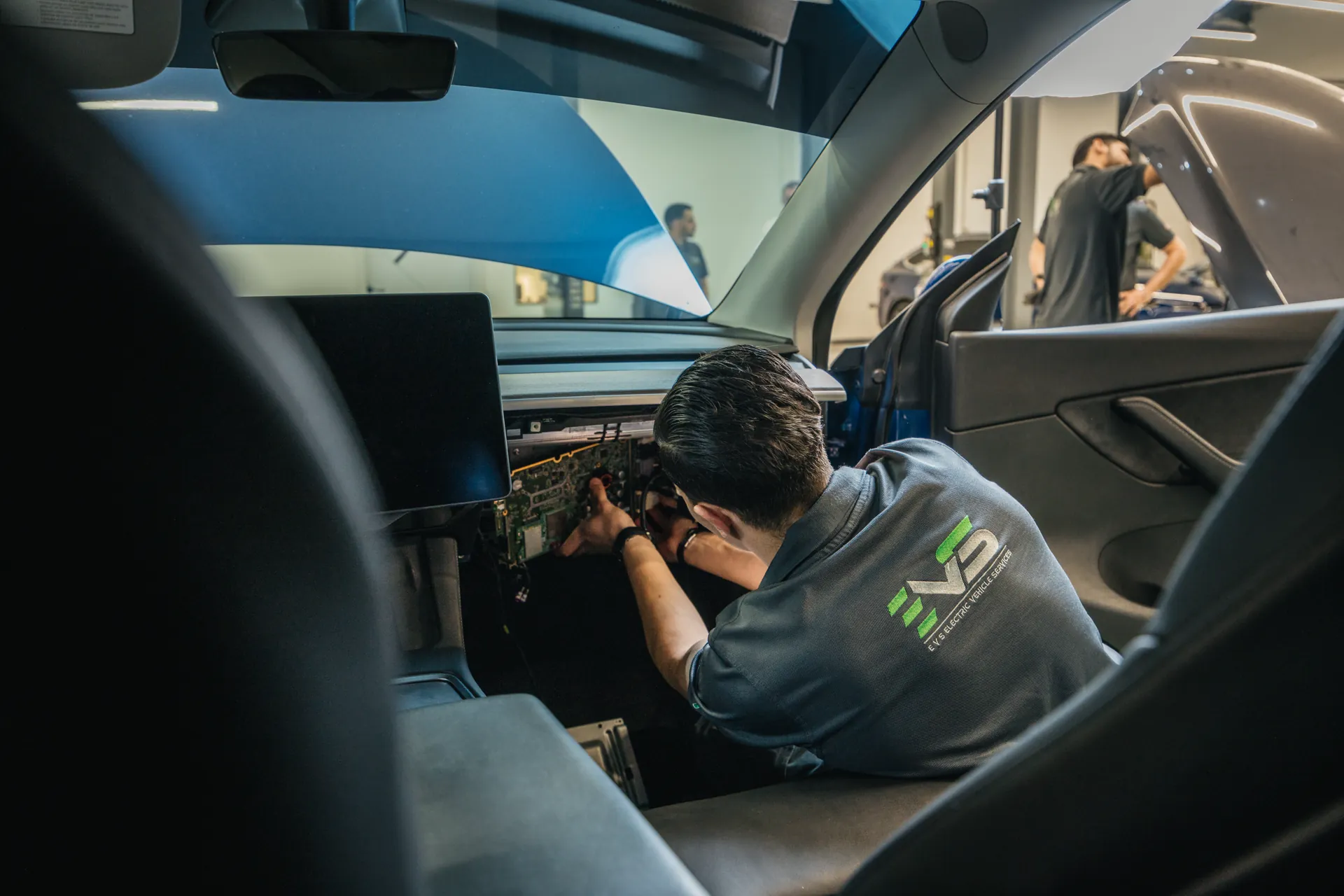 An EVS technician working on the dashboard electronics of an electric car