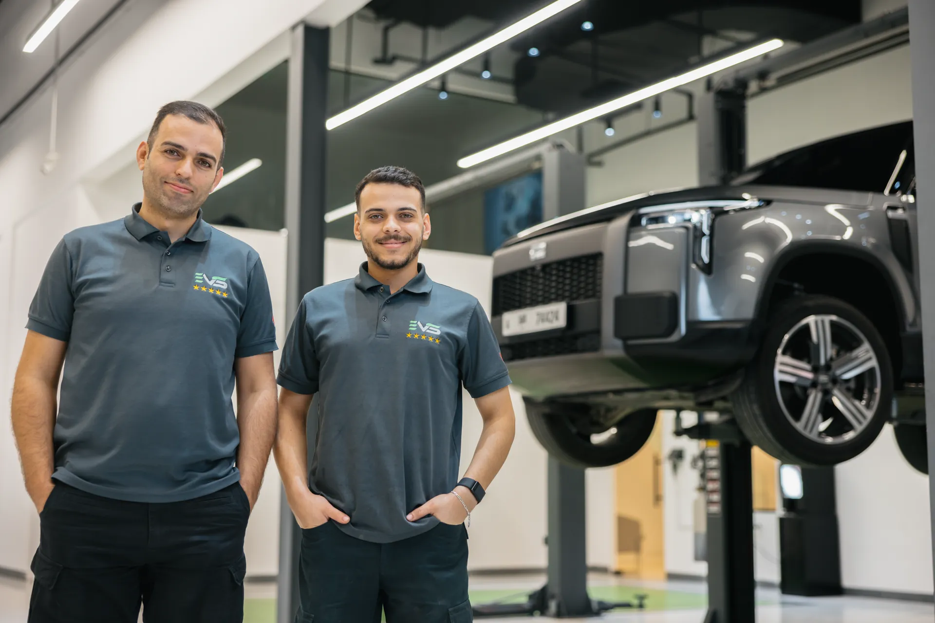 Two EVS technicians in the workshop beside an electric SUV raised on a lift